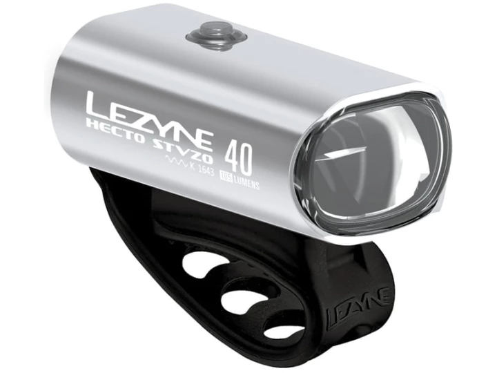 In unserem Online-Fahrradshop ist ein silbernes Lezyne Hecto Drive 40 StVZO-Fahrradlicht mit schwarzem Gummi-Befestigungsband erhältlich. Dieses rechteckige Licht verfügt über eine einzelne Linse auf der Vorderseite und einen Markentext an der Seite. Das Befestigungsband ist praktischerweise an der Unterseite angebracht.