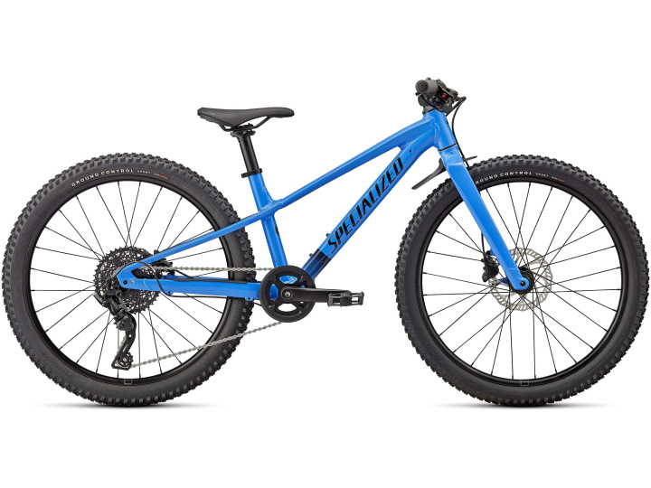 Das Specialized Riprock 24 ist ein leuchtend blaues Jugend-Mountainbike mit stabilem Rahmen, schwarzem Lenker und schwarzem Sattel. Es verfügt über Scheibenbremsen vorne und hinten, eine verstärkte Kette und Stollenreifen für unwegsames Gelände. Der Markenname ist auf der Mittelstange des Rahmens sichtbar. Erhältlich in Ihrem örtlichen Fahrradladen.