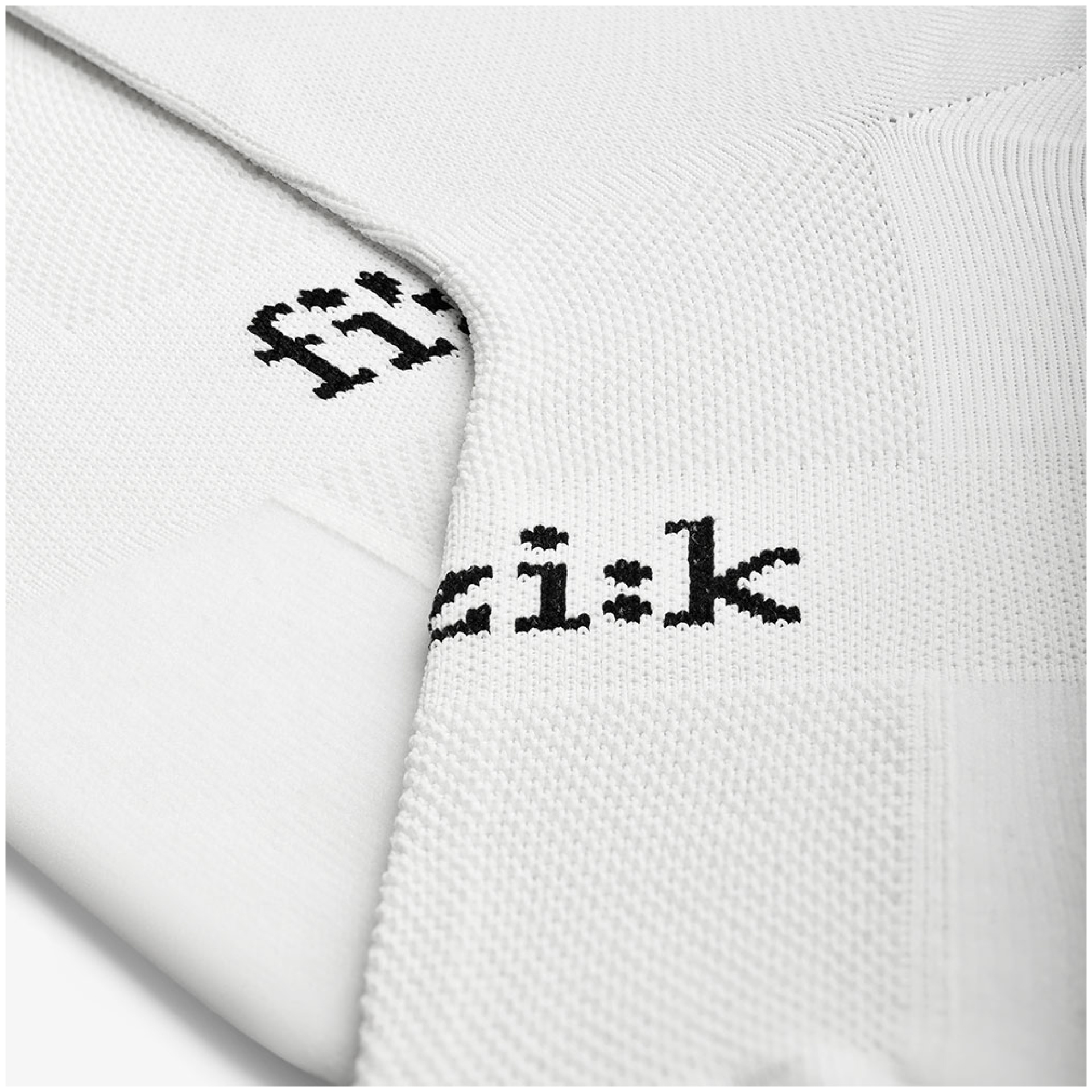 Nahaufnahme der FIZIK SOCKEN RENNRAD. Der weiße strukturierte Stoff mit dem schwarzen Text „fizik“ in kleiner, minimalistischer Schrift ist zu sehen. Der Stoff weist ein gestricktes oder gewebtes Muster mit unterschiedlichen Texturen auf. Der Text wird auf dem sichtbaren Teil der Socke zweimal wiederholt.