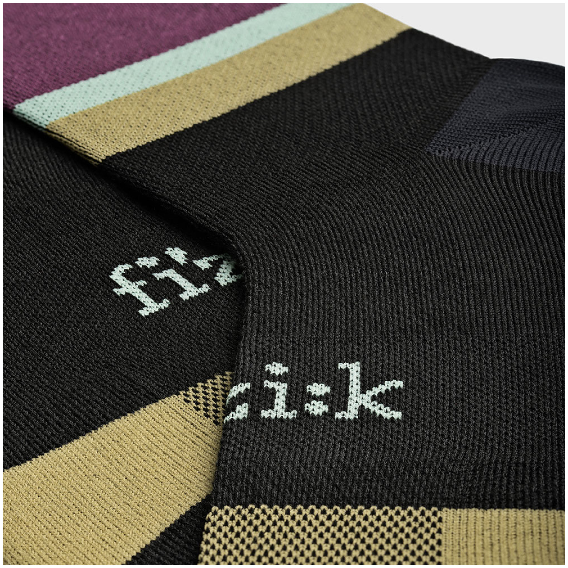 Nahaufnahme der schwarzen Socken FIZIK SOCKEN TEAM mit aufwendigen Strickmustern und dem „fi'zi:k“-Logo in Weiß. Die Oberseite der Socken weist einen kontrastierenden beige- und kastanienbraunen Streifen auf, der das Design hervorhebt. Die Textur des Stoffes ist deutlich sichtbar.