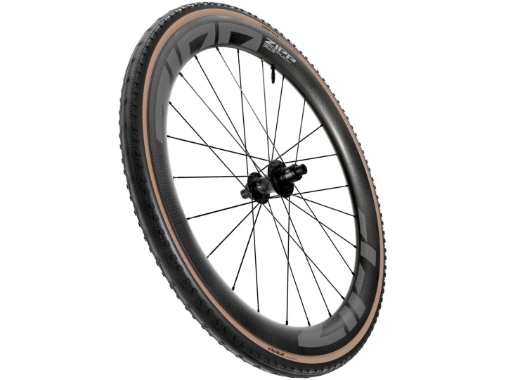 Der ZIPP Reifen Goodyear SLICK XPLR ist ein Hochleistungs-Fahrradrad mit einer Carbonfaserfelge, schwarzen Speichen und einer schwarzen Nabe. Es verfügt über einen Reifen mit hellbrauner Seitenwand und Profilmuster, was darauf hindeutet, dass er für das Rennradfahren konzipiert ist. Das Rad scheint einen Aufwärtswinkel zu haben.