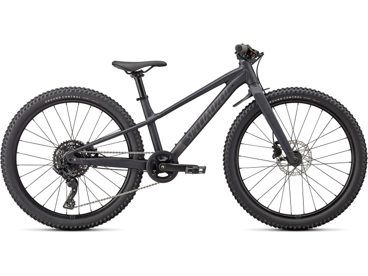 Das Specialized Riprock 24, ein schwarzes Mountainbike mit dicken Stollenreifen, einem stabilen Rahmen, Scheibenbremsen vorne und hinten und einem einzelnen Kettenblatt vorne, ist von der Seite vor einem weißen Hintergrund abgebildet.