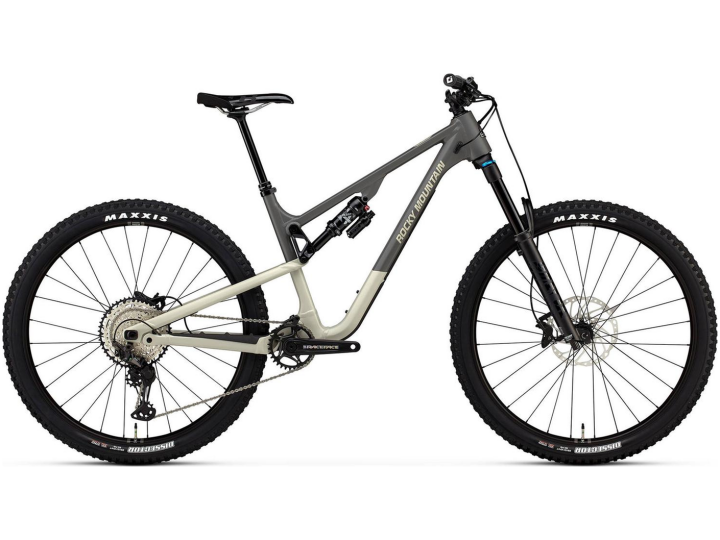 Das Rocky Mountain Instinct Alloy 50 ist ein vollgefedertes Mountainbike mit grau-beigem Rahmen, schwarzem Sattel, schwarzem Lenker und großen Maxxis-Reifen, von der Seite auf weißem Hintergrund abgebildet.