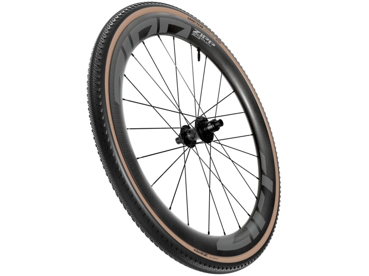 Das ZIPP Reifen Goodyear INTER XPLR hat einen dicken hellbraunen Reifen mit Seitenwand, eine tiefe Kohlefaserfelge, schwarze Speichen und eine Scheibenbremsnabe, die schräg vor einem weißen Hintergrund steht.