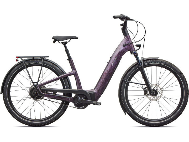 Das Specialized Como 4.0 IGH, ein lilafarbenes Elektrofahrrad mit Durchstiegsrahmen, schwarzem Sitz, breiten Reifen, Scheibenbremsen und Gepäckträger, wird im Seitenprofil auf einem schlichten weißen Hintergrund gezeigt.