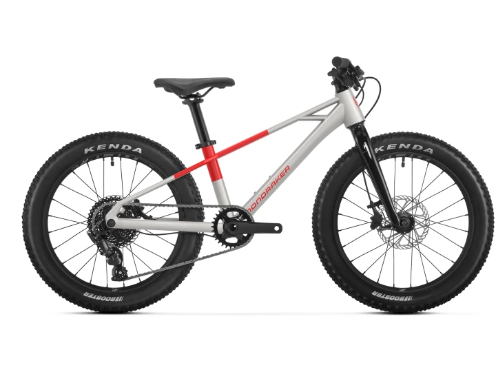 Das Mondraker Trick 20 ist ein silber-rotes Kinder-Mountainbike mit dicken schwarzen Kenda-Reifen, Federgabel, flachem Lenker und stabilem Rahmen, das im Profil auf weißem Hintergrund abgebildet ist.