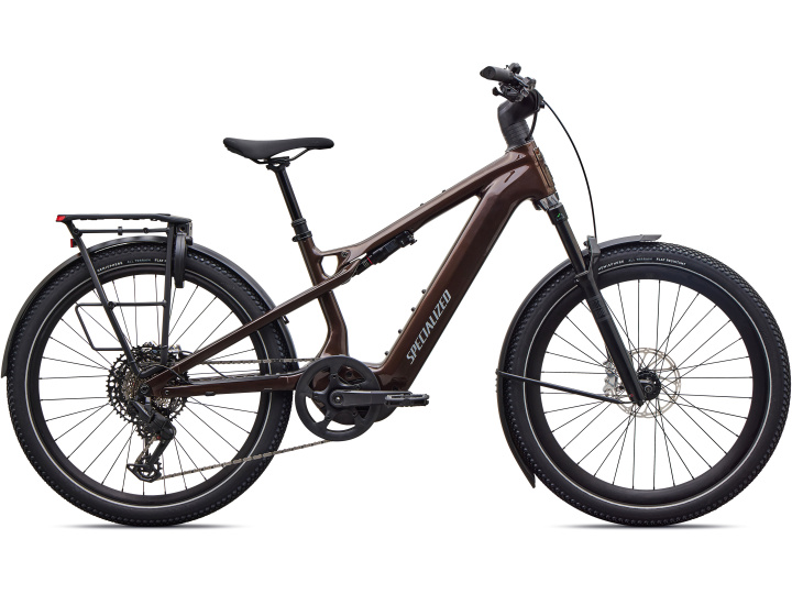 Ein braunes Specialized Vado 3 X 5.0 E-Bike mit breiten Reifen, einer Vorderrad-Federgabel, einem Gepäckträger hinten und einem schräg verlaufenden Oberrohr ist in der Seitenansicht vor einem weißen Hintergrund abgebildet.