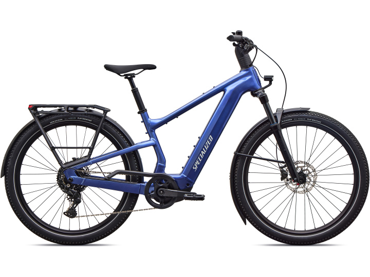 Ein blaues Specialized Turbo Vado 3 EVO 4.0-Elektrofahrrad mit Gepäckträger, vorderen und hinteren Schutzblechen, Scheibenbremsen und breiten Reifen ist im Profil vor einem weißen Hintergrund abgebildet.
