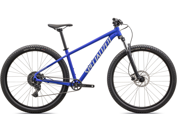 Das Specialized Rockhopper Sport, ein blaues Mountainbike mit großen Stollenreifen, Scheibenbremsen, einem flachen Lenker und einem leichten Rahmen, ist im Seitenprofil vor weißem Hintergrund abgebildet.
