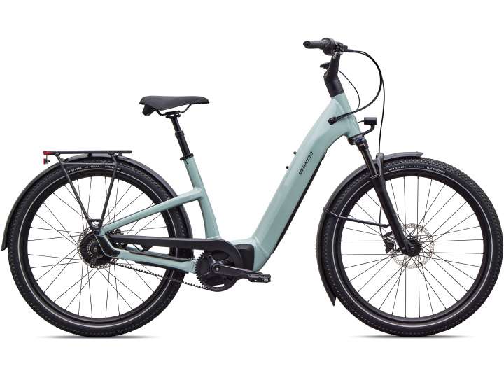 Das Specialized Como 4.0 IGH NB ist ein hellblaues E-Bike mit tiefem Einstieg, das über eine Vorderradfederung, einen Gepäckträger hinten und breite schwarze Reifen verfügt und hier von der Seite vor einem weißen Hintergrund zu sehen ist.