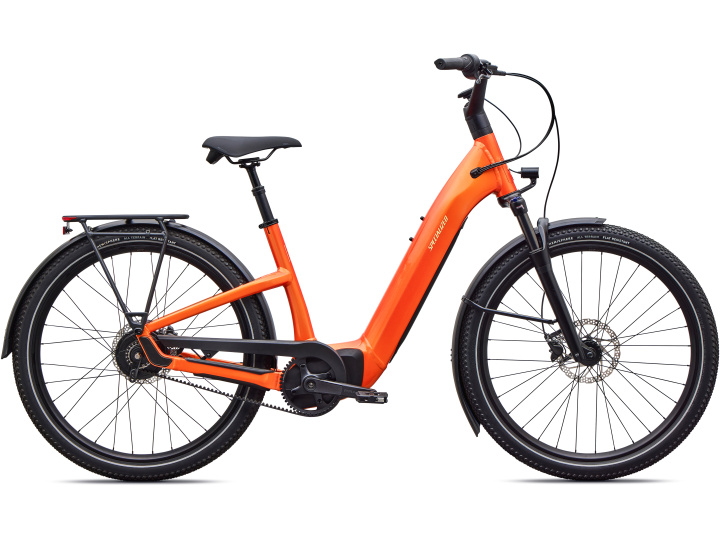 Das Specialized Como 4.0 IGH NB ist ein orangefarbenes E-Bike mit tiefem Einstieg, das mit schwarzen Reifen, Schutzblechen, einem Gepäckträger und einem bequemen Sattel ausgestattet ist und hier von der Seite vor einem weißen Hintergrund zu sehen ist.