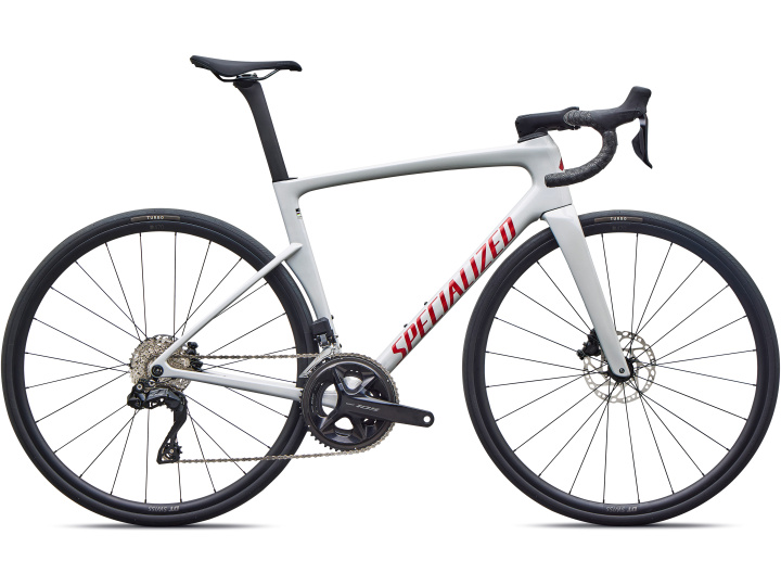 Ein weißes Specialized Tarmac SL9 Comp-Rennrad mit Drop-Lenker, schmalen Reifen, Scheibenbremsen und einem roten „SPECIALIZED“-Logo auf dem Rahmen, im Profil auf weißem Hintergrund abgebildet.